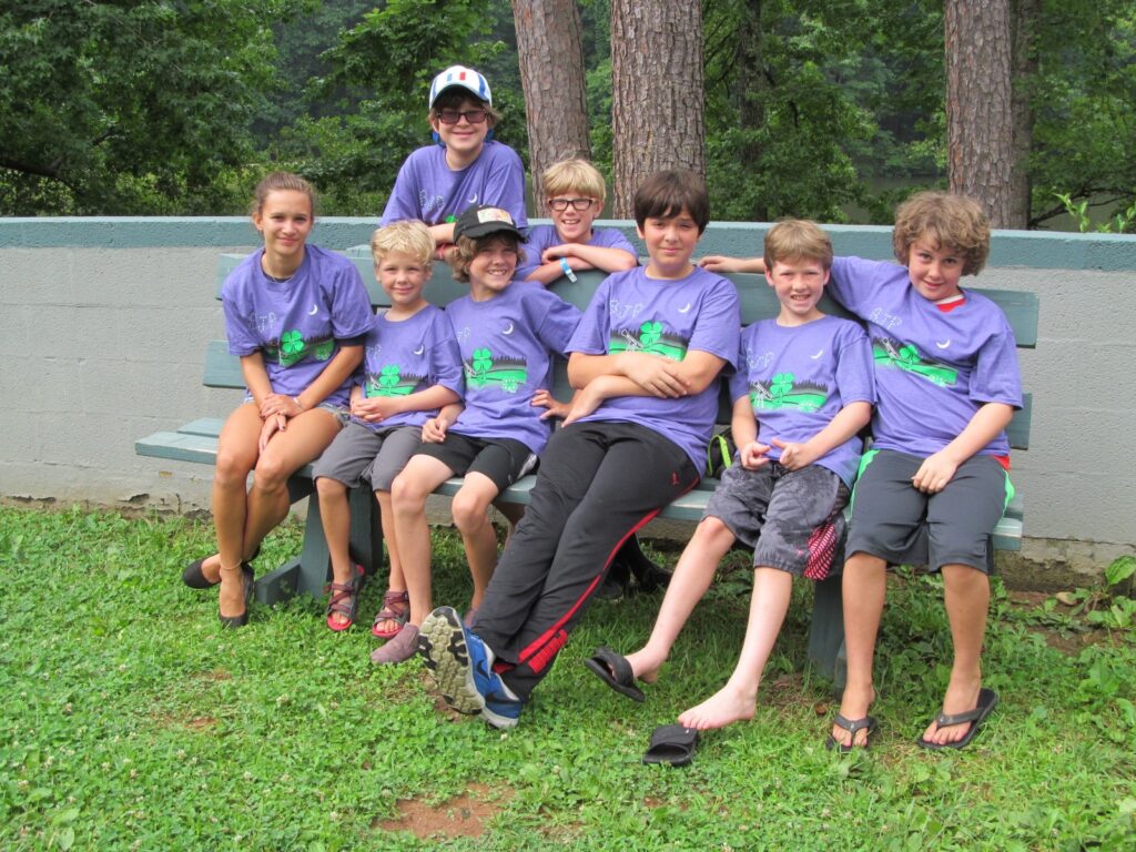 A group of children in matching shits sit on a bench together. 