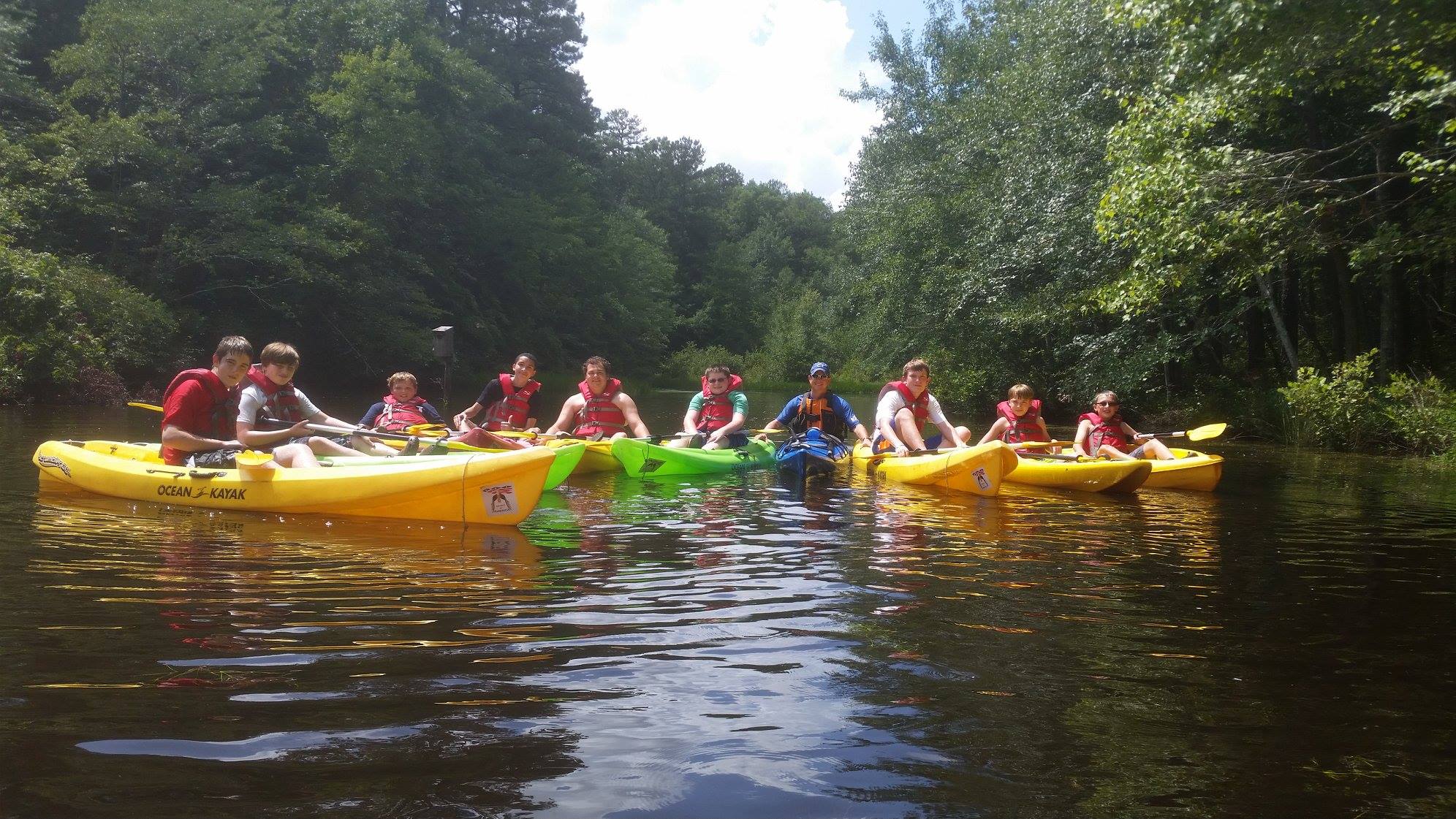 Adults with a group of kids kayaking down a river.