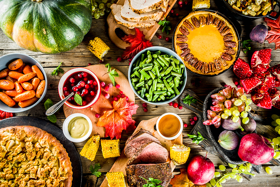 table spread with fall foods, pies, fruits, ham, squash, cranberries, corn