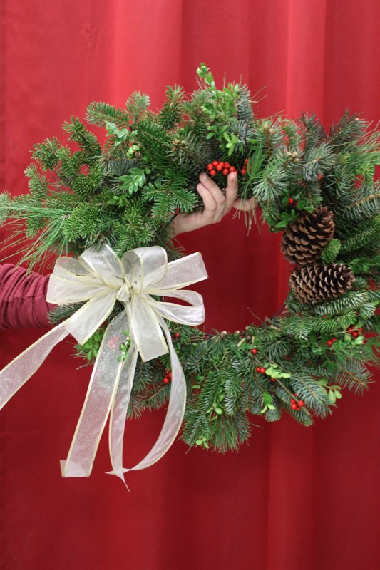 A Christmas wreath held in front of a red curtain.